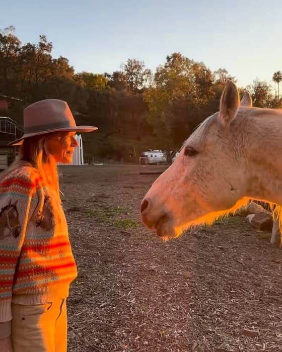Lara Plutte in a felt hat at golden hour, face to face with a cremello horse
