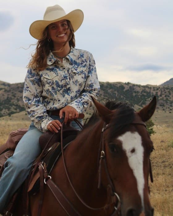 Olivia Autore in a wide hat, mounted on a bay horse in open hill country