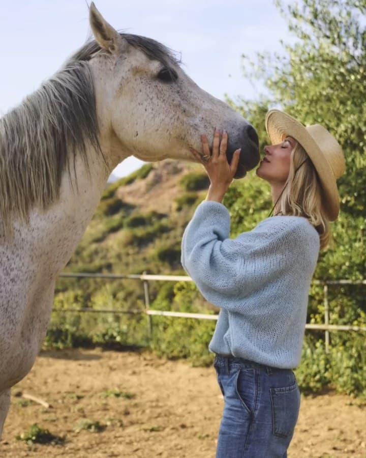 Rose Mary Riggs in a straw hat, face to face with a grey horse on the hillside